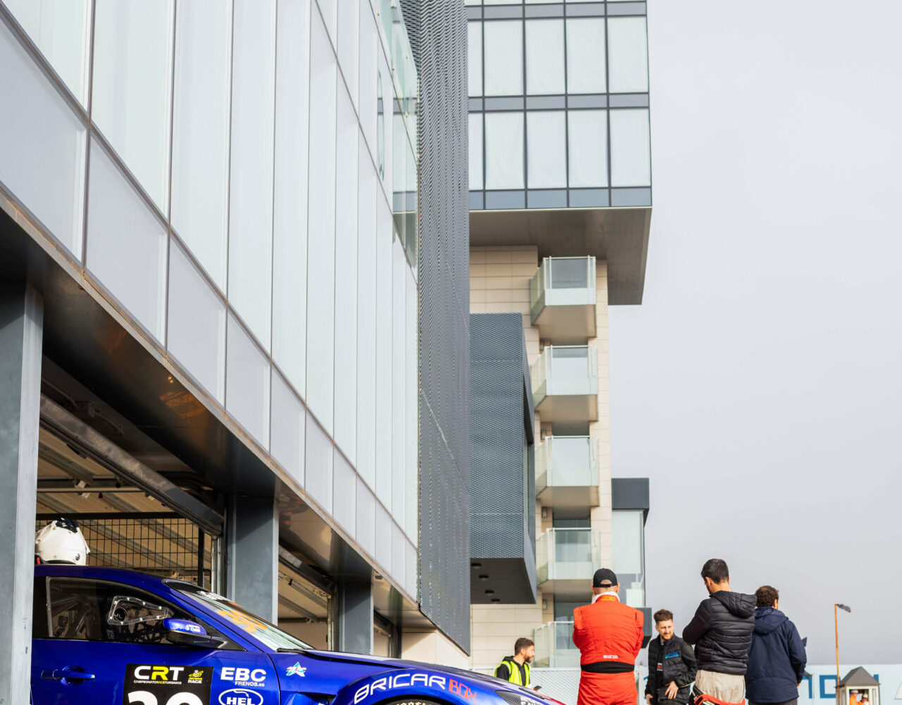 Mazda RX8 en el box con mecánicos y pilotos cerca de él y la torre del Jarama de fondo en el Campeonato Race de Turismos 2023. Fotografía de Warmedia