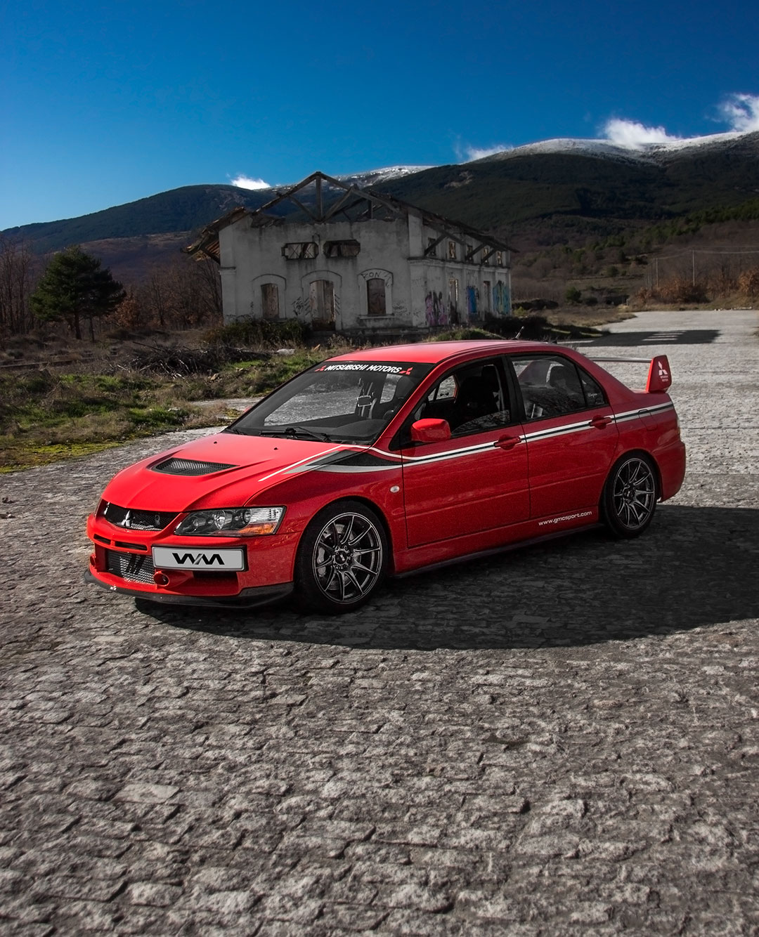 Fotografía de 3_4 de Mitsubishi lancer evo IX de color rojo con vinilo de color negro y gris con parasol de Mitsubishi motors. En el fondo está la vieja estación de Gascones-Buitrago. Fotografía propiedad de Warmedia Fotografía