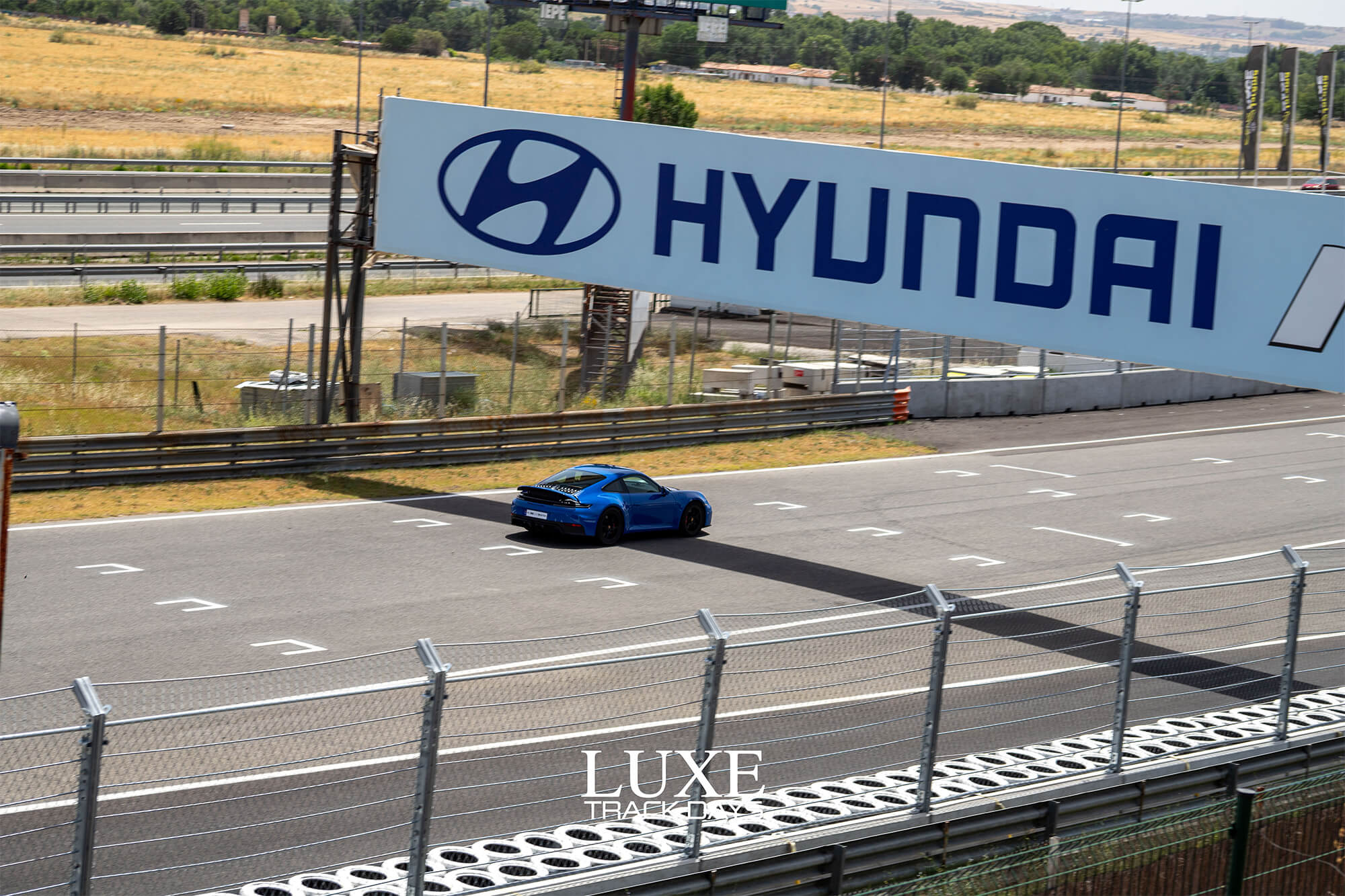 Porsche 911 azul pasando bajo el puente Hyundai del Circuito del Jarama